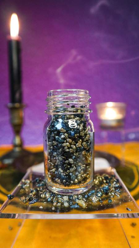 Räucherwerk Fast Luck im 30ml Glas auf durchsichtigem Podest mit brennenden Kerzen im Hintergrund