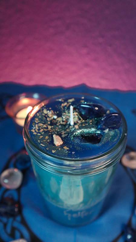 Ritualglaskerze Entscheidungshelfer mit Sodalith Glitzer und Kräuter mit brennendem Teelicht im Hintergrund