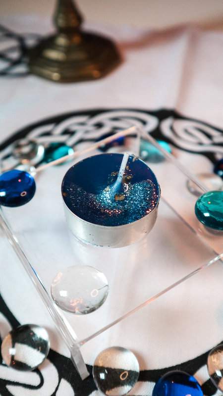 Teekerze Geistesblitz blau mit Glitzer auf durchsichtigem Podest mit Deko aus Glasperlen