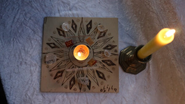 Brennende Teekerze Lichtblick für Zuversicht und positive Energie mit Glasrunen auf Holzboard neben einer Stabkerze