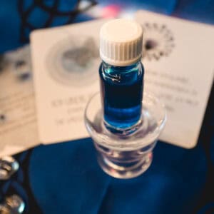 Anna Riva Öl auf Glaskerzenhalter und blauem Untergrund mit Motivationskarten und Glasnuggets als Deko